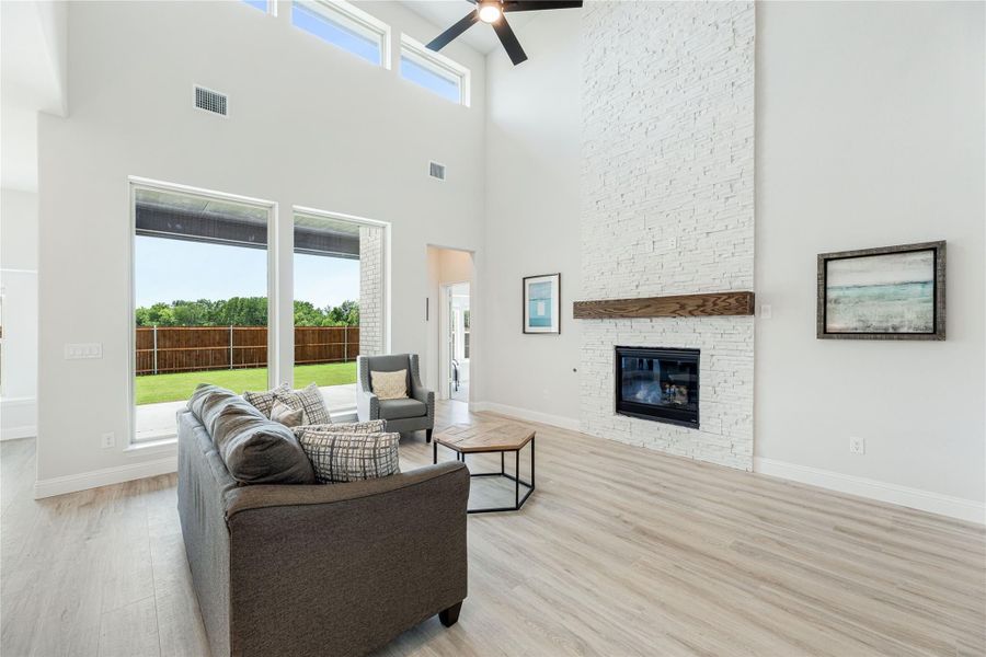 Living room with two-story ceiling, white stone fireplace, and large windows overlooking backyard