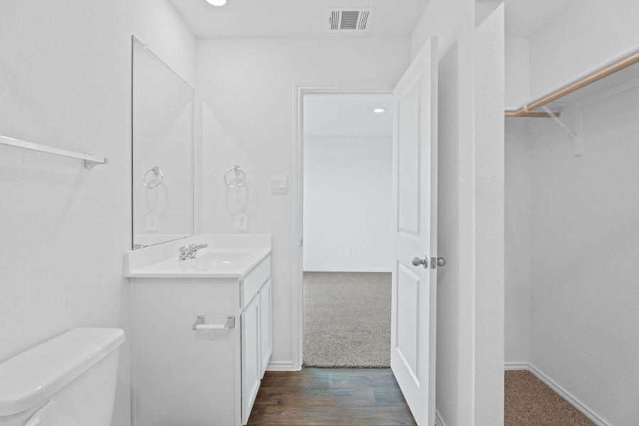 Bathroom featuring toilet, visible vents, vanity, wood finished floors, and a spacious closet Bathroom featuring toilet, visible vents, vanity, wood finished floors, and a spacious closet