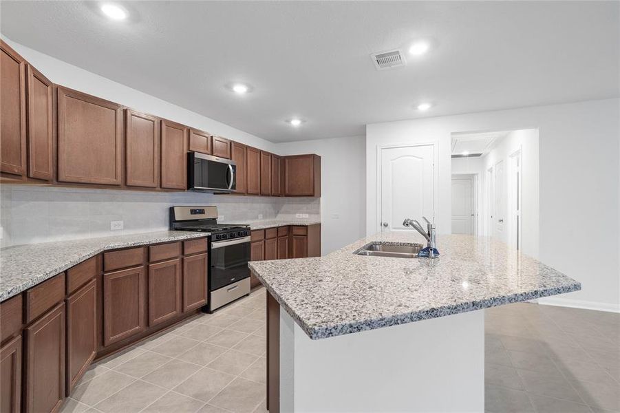 Another view of this beautiful kitchen showcasing the stainless steel Whirlpool gas range and microwave, and the granite countertop with modern tile backsplash.