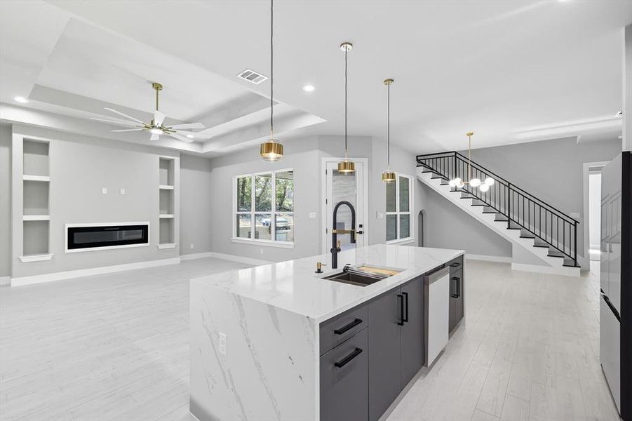 Kitchen featuring a tray ceiling, pendant lighting, a ceiling fan, light wood-type flooring, and an island with sink