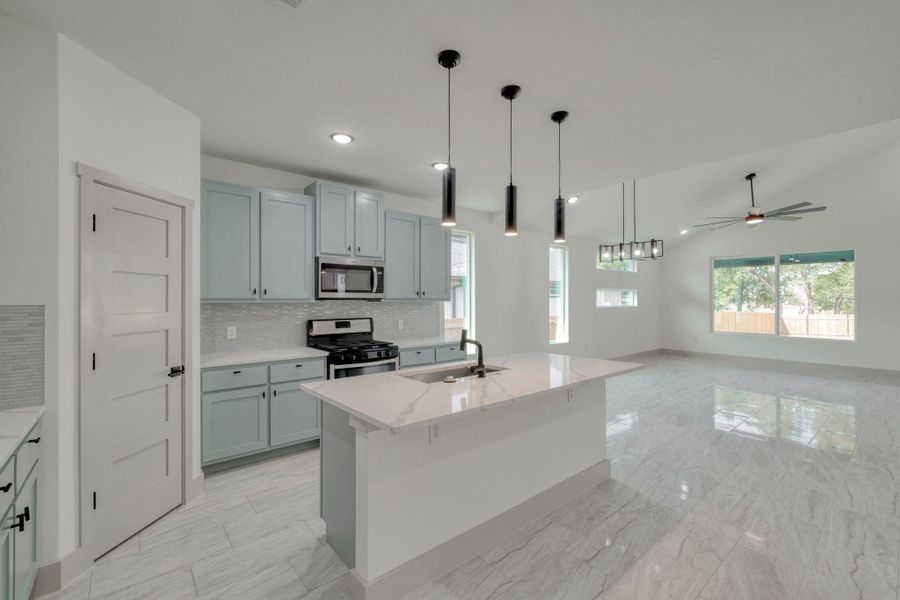 Kitchen with decorative backsplash, pendant lighting, light stone counters, appliances with stainless steel finishes, and a kitchen island you can sit at with sink Kitchen with decorative backsplash, pendant lighting, light stone counters, appliances with stainless steel finishes, and a kitchen island you can sit at with sink