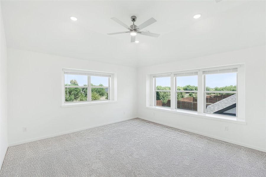 Empty bedroom with gray carpet, ceiling fan, and multiple windows with outdoor views