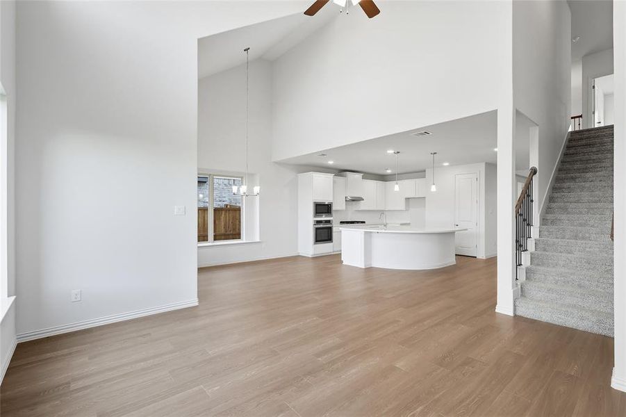Unfurnished living room with stairs, high vaulted ceiling, ceiling fan, light wood-style floors, and a chandelier Unfurnished living room with stairs, high vaulted ceiling, ceiling fan, light wood-style floors, and a chandelier