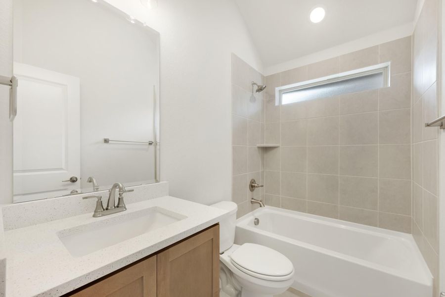Bathroom with quartz vanity, wood cabinets, and tiled shower-tub combo with small window Bathroom with quartz vanity, wood cabinets, and tiled shower-tub combo with small window