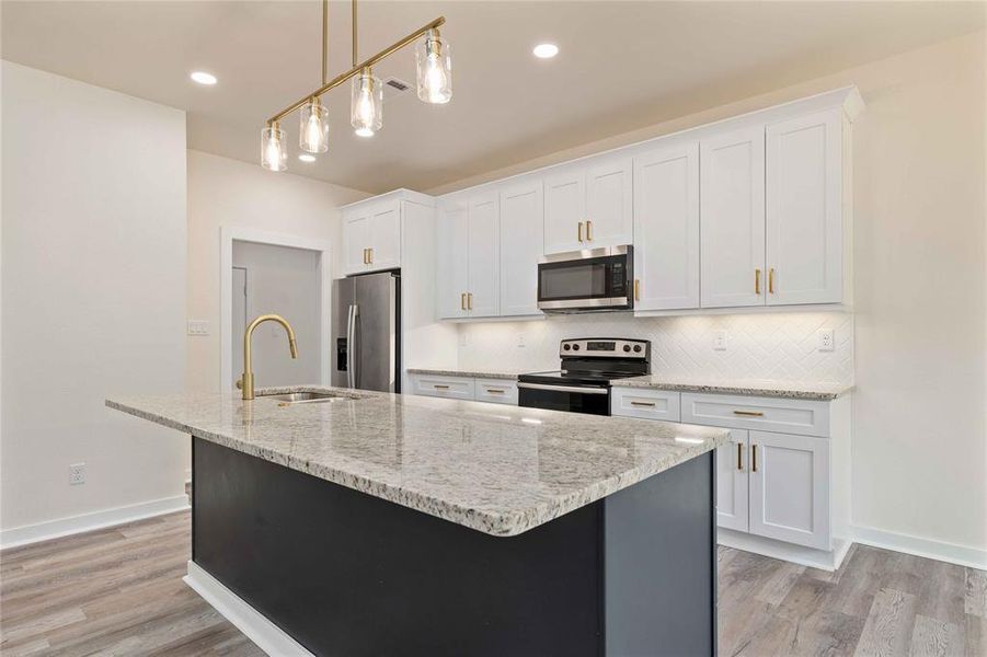 Kitchen with hanging light fixtures, light stone countertops, appliances with stainless steel finishes, backsplash, and a kitchen island with sink Kitchen with hanging light fixtures, light stone countertops, appliances with stainless steel finishes, backsplash, and a kitchen island with sink