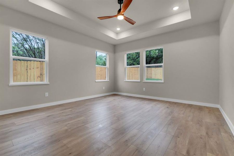 Unfurnished room with a raised ceiling, ceiling fan, and light wood-type flooring