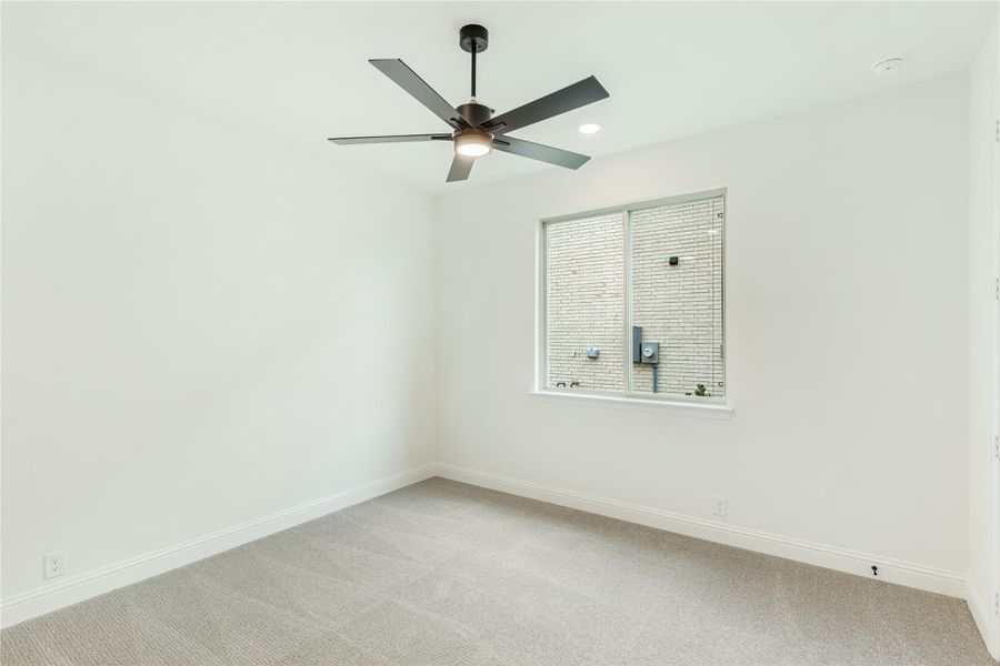 Empty bedroom with white walls, gray carpet, ceiling fan, and single window
