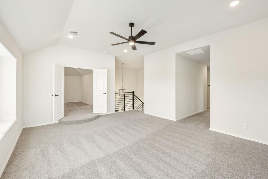 Spacious upstairs loft with vaulted ceiling, ceiling fan, carpet flooring, and open staircase railing