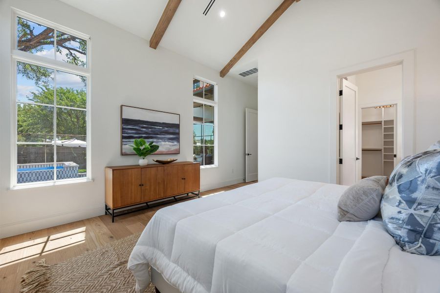 Vaulted ceilings with exposed wood beams elevate this light-filled bedroom featuring wide-plank hardwood floors.
