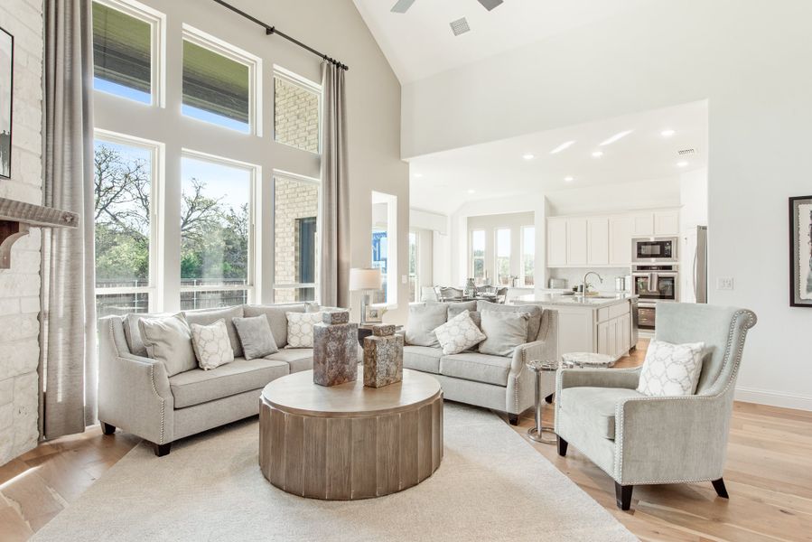 Open-concept living room with vaulted ceiling, tall windows, gray sofas, and kitchen visible in background Open-concept living room with vaulted ceiling, tall windows, gray sofas, and kitchen visible in background