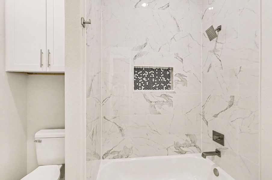 Stylish secondary bath with marble-look tile surround and modern fixtures.