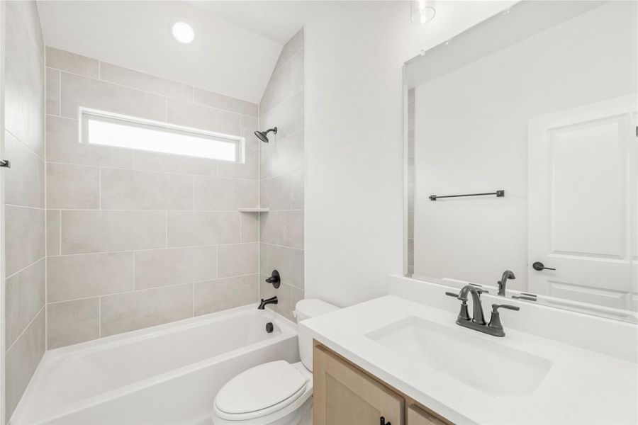 Full bathroom with tiled tub-shower combo, white vanity, and dark hardware fixtures