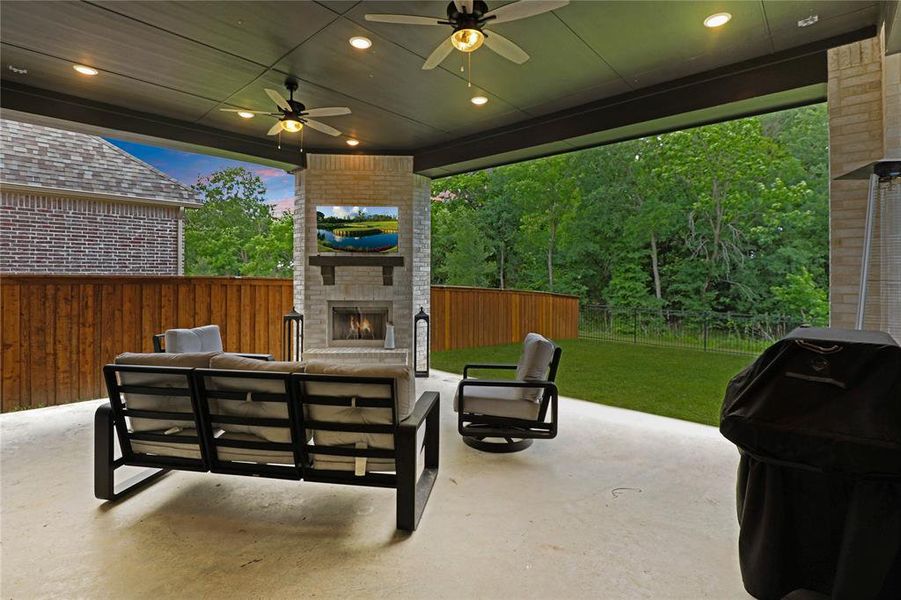 Spacious covered patio featuring a brick fireplace with a wood mantel, overhead lighting, and ceiling fans