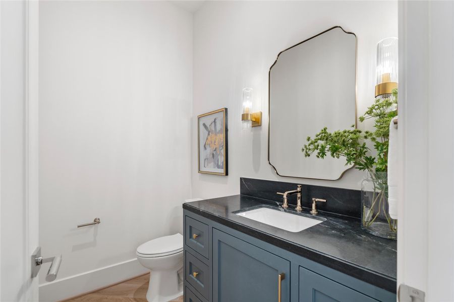 The second-floor powder bath is decorated with honed quartzite countertops, gold, polished gold finishes, and dark cabinetry. A second-floor powder rooms is is idea for entertaining in the adjacent media room.
