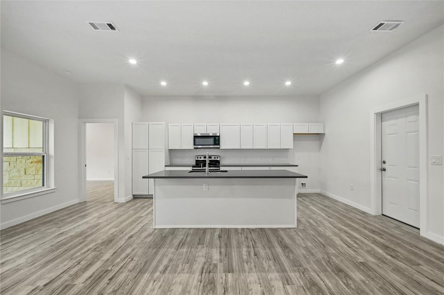 Kitchen with dark countertops, white cabinets, recessed lighting, stainless steel appliances, and a kitchen island with sink