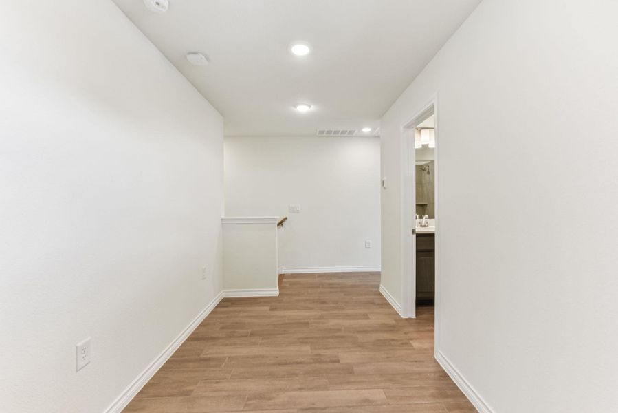 Hall with light wood finished floors, recessed lighting, and an upstairs landing Hall with light wood finished floors, recessed lighting, and an upstairs landing