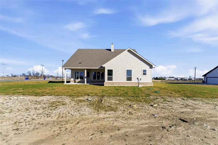 Back of house featuring a patio, a chimney, a yard, and a shingled roof