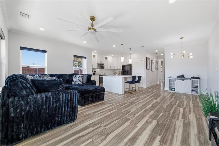 Living area with wood finish floors, crown molding, ceiling fan, and hanging lights