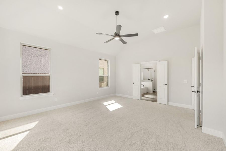 Spacious bedroom with ceiling fan, carpet flooring, and ensuite bathroom access