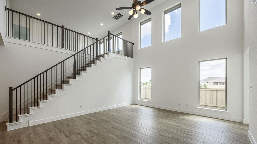 Unfurnished living room with a towering ceiling, a ceiling fan, stairway, wood finished floors, and recessed lighting Unfurnished living room with a towering ceiling, a ceiling fan, stairway, wood finished floors, and recessed lighting