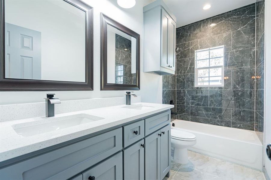 Full bathroom with tile patterned floors, double sink vanity, tiled shower / bath combo, and toilet