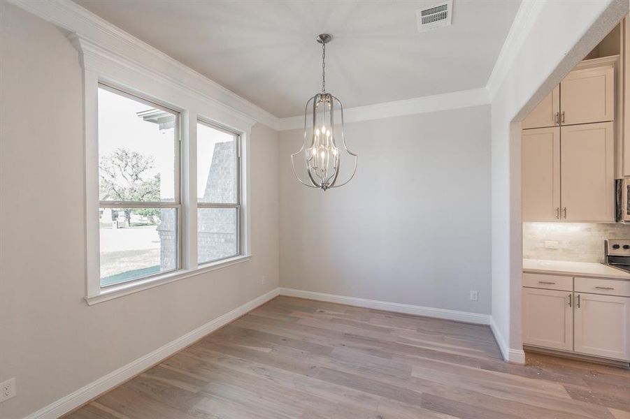 Unfurnished dining area featuring light wood-type flooring, an inviting chandelier, and crown molding