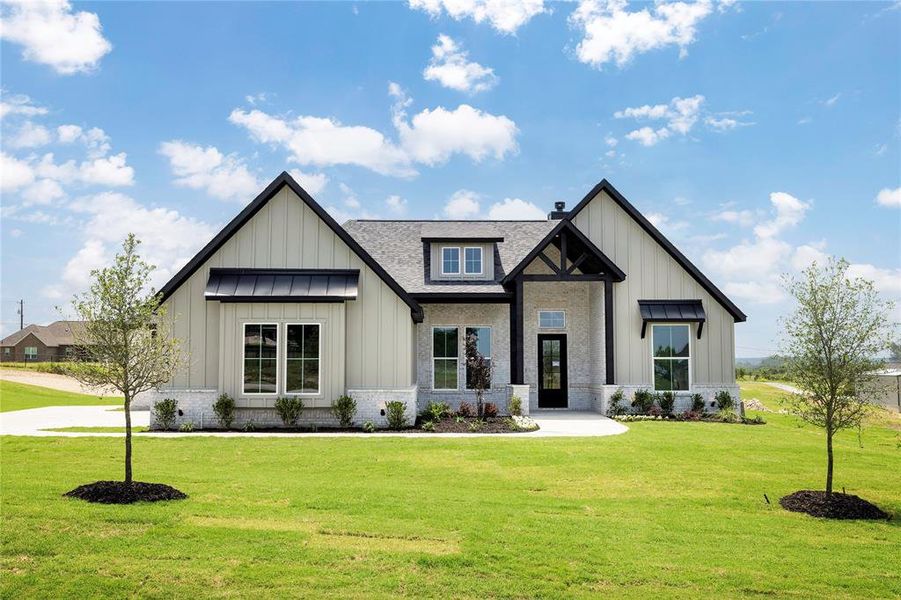 View of front of home with board and batten siding, a front lawn, roof with shingles, and brick siding