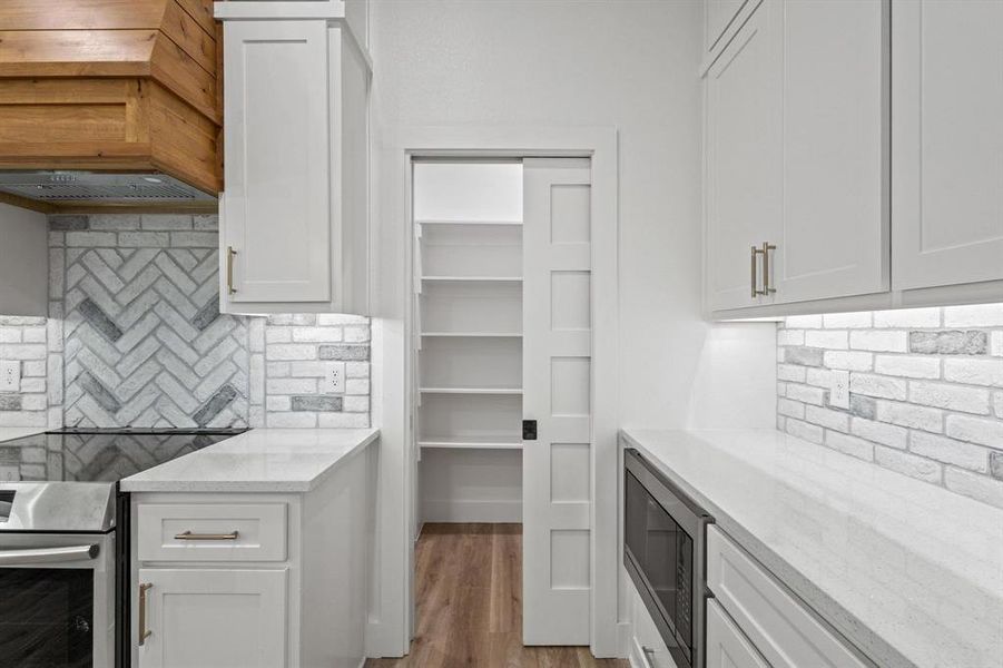Kitchen with light stone counters, white cabinetry, tasteful backsplash, built in microwave, and stainless steel range oven