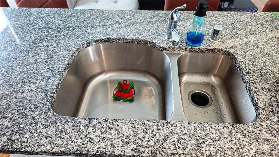 Granite countertop surrounding a stainless steel double basin sink with a chrome faucet