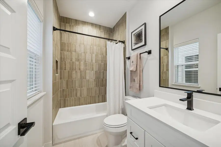 Guest bathroom featuring a deep soaking tub surrounded by vertical tile, a modern vanity with matte black fixtures, and a bright window that fills the space with natural light. Guest bathroom featuring a deep soaking tub surrounded by vertical tile, a modern vanity with matte black fixtures, and a bright window that fills the space with natural light.