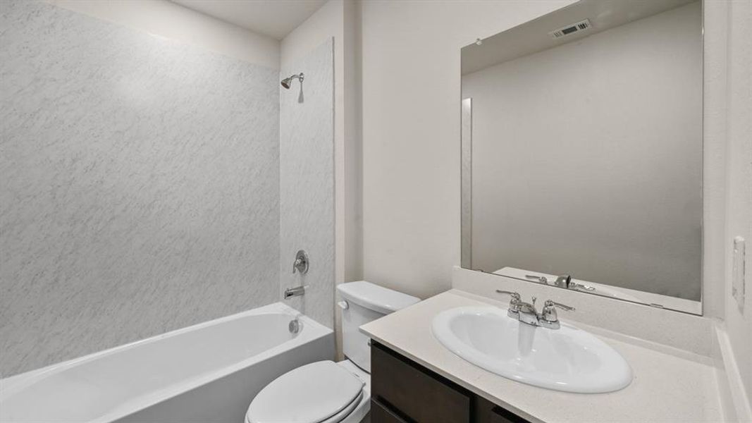 Bathroom featuring a white bathtub, shower with white textured surround, dark wood vanity with a light countertop, and a large wall-mounted mirror Bathroom featuring a white bathtub, shower with white textured surround, dark wood vanity with a light countertop, and a large wall-mounted mirror