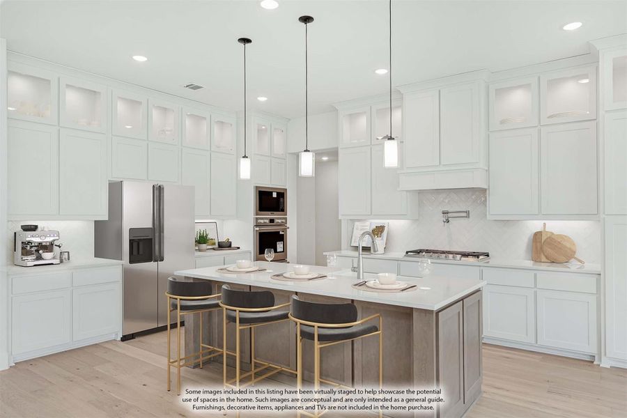 White kitchen with tall cabinets, center island with seating, stainless appliances, and pendant lights over light wood floors