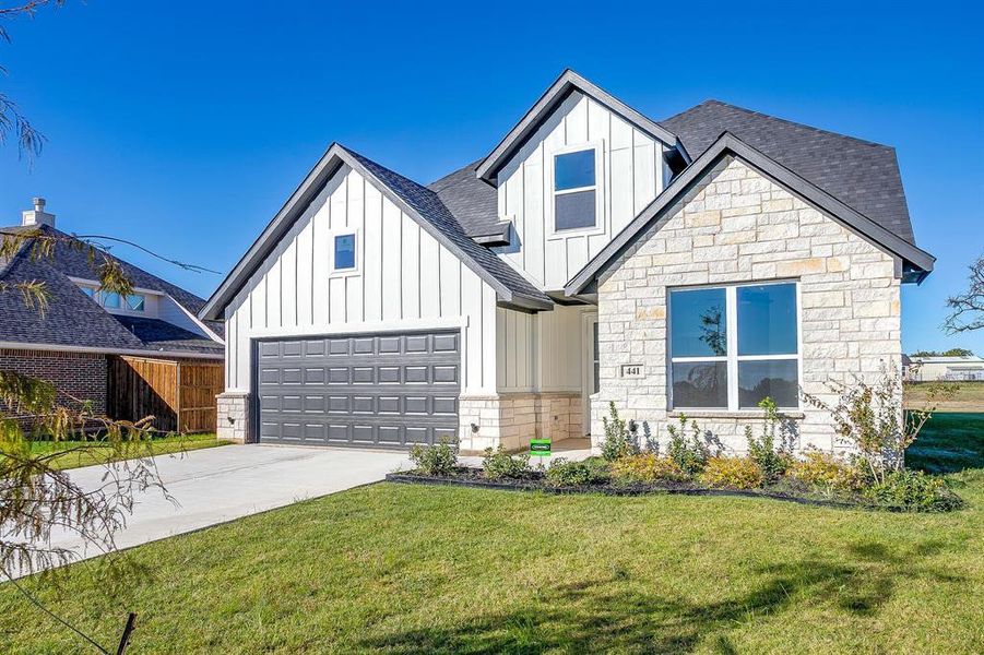 View of front of house featuring board and batten siding, driveway, roof with shingles, and stone siding