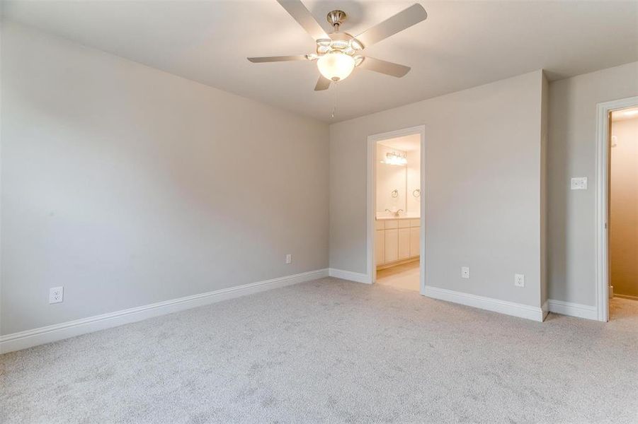 Unfurnished bedroom featuring ceiling fan, ensuite bath, and light carpet