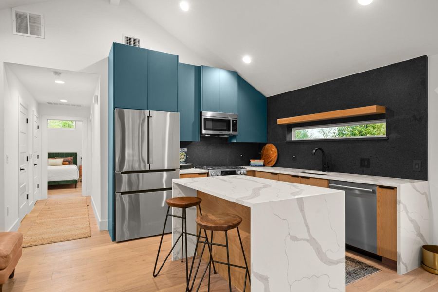 Kitchen with stainless steel appliances, light stone countertops, lofted ceiling, a breakfast bar area, and a center island