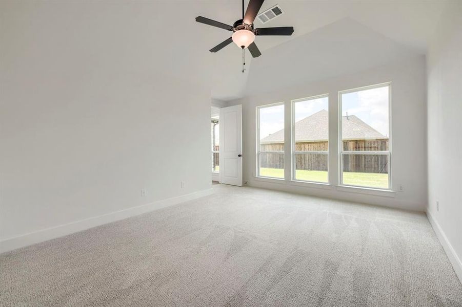 Bright room featuring three large windows, a vaulted ceiling, a ceiling fan with light fixture, and plush carpeting Bright room featuring three large windows, a vaulted ceiling, a ceiling fan with light fixture, and plush carpeting