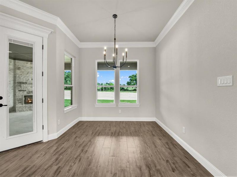 Unfurnished dining area with a chandelier, dark wood-type flooring, baseboards, crown molding, and a fireplace Unfurnished dining area with a chandelier, dark wood-type flooring, baseboards, crown molding, and a fireplace