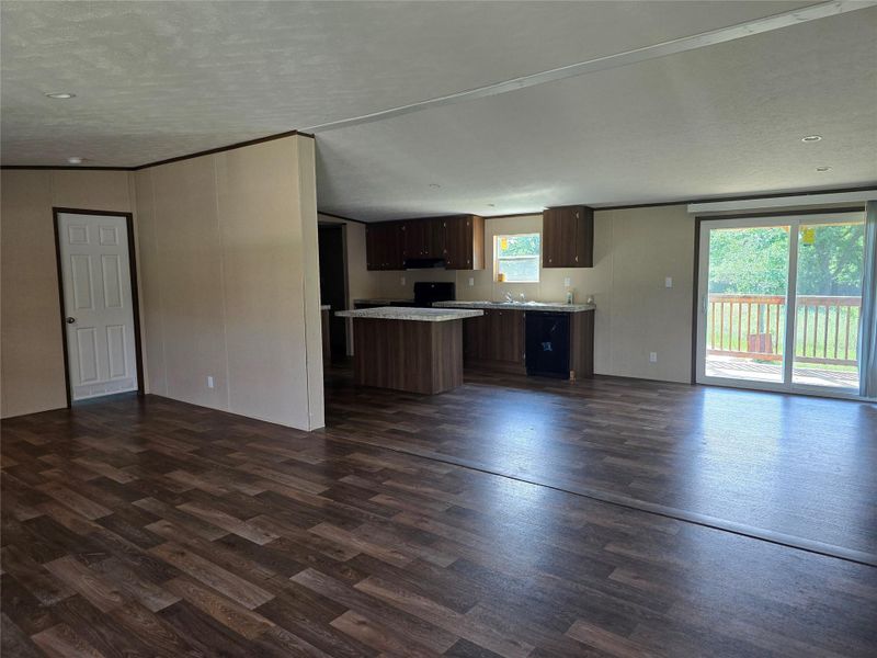 Spacious interior featuring wood-finish flooring, a kitchen with dark cabinetry, and a center island with a light-colored countertop Spacious interior featuring wood-finish flooring, a kitchen with dark cabinetry, and a center island with a light-colored countertop