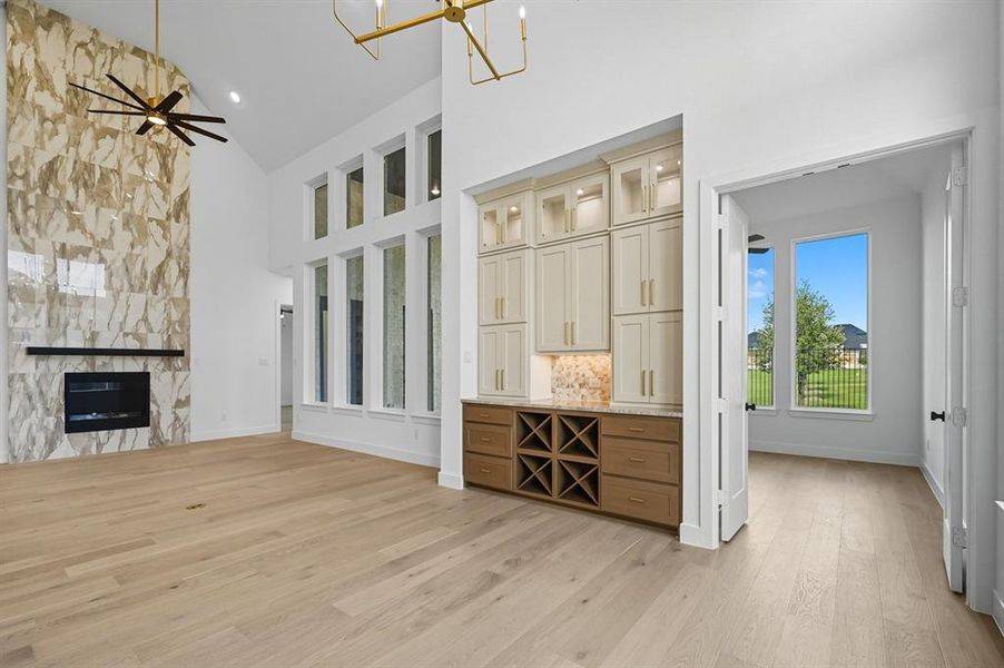 Unfurnished living room featuring a large fireplace, ceiling fan, light wood-style floors, high vaulted ceiling, and a chandelier Unfurnished living room featuring a large fireplace, ceiling fan, light wood-style floors, high vaulted ceiling, and a chandelier