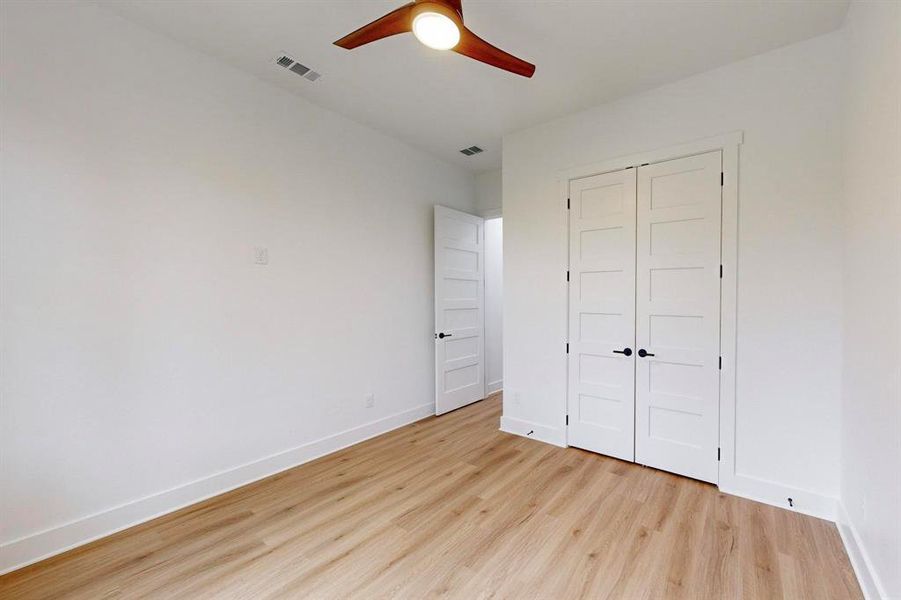 Interior room featuring light wood-finish flooring, white walls, and a ceiling fan with wood-tone blades Interior room featuring light wood-finish flooring, white walls, and a ceiling fan with wood-tone blades
