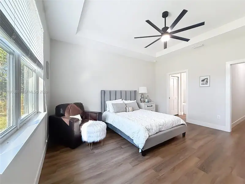 Bedroom featuring a tray ceiling, multi-blade ceiling fan, wood-finish flooring, and large windows with blinds