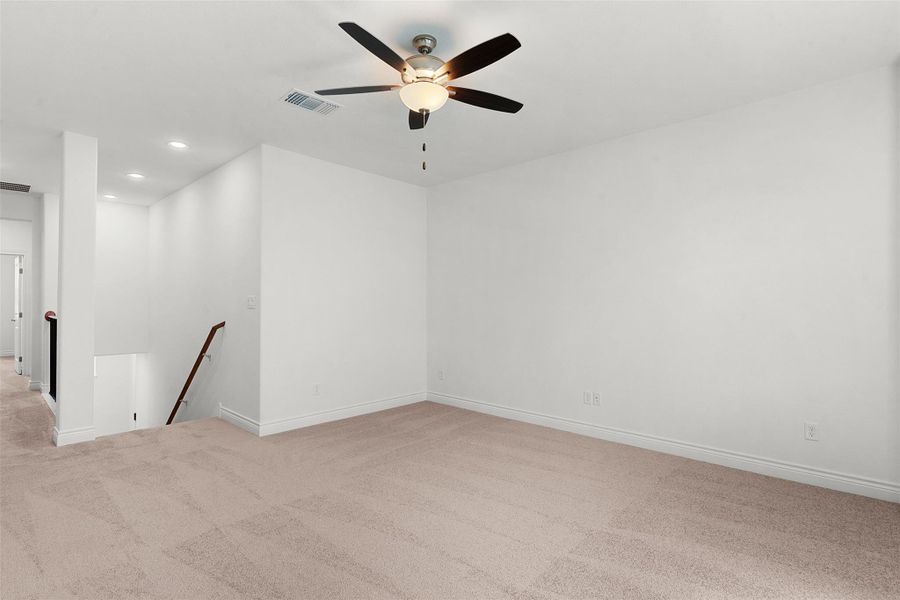 Neutral-toned carpeting extends throughout this open room, featuring a ceiling fan with integrated lighting