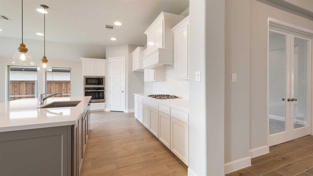 Kitchen with white cabinetry, sink, a center island with sink, custom range hood, and appliances with stainless steel finishes