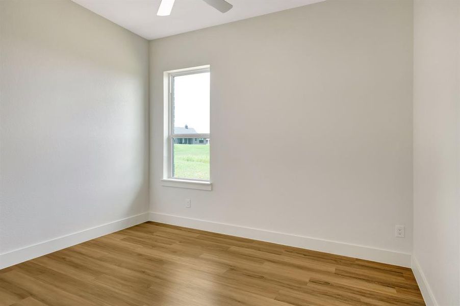 Bright interior space featuring a window with natural light, wood-finish flooring, white baseboards, and a ceiling fan Bright interior space featuring a window with natural light, wood-finish flooring, white baseboards, and a ceiling fan