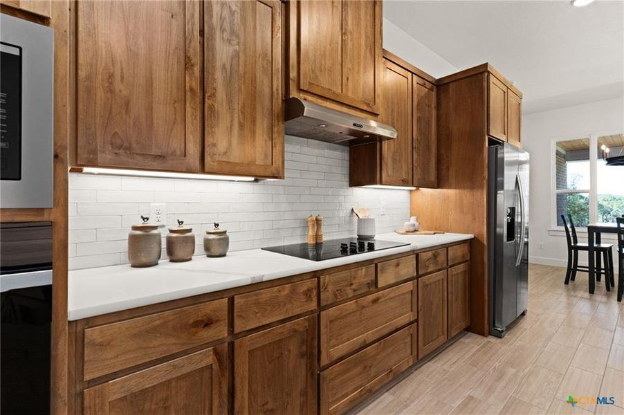 Kitchen featuring light countertops, brown cabinets, decorative backsplash, and stainless steel appliances