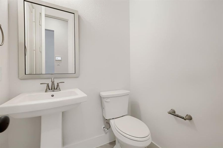 Pedestal sink with a brushed nickel faucet, framed mirror, and white toilet Pedestal sink with a brushed nickel faucet, framed mirror, and white toilet