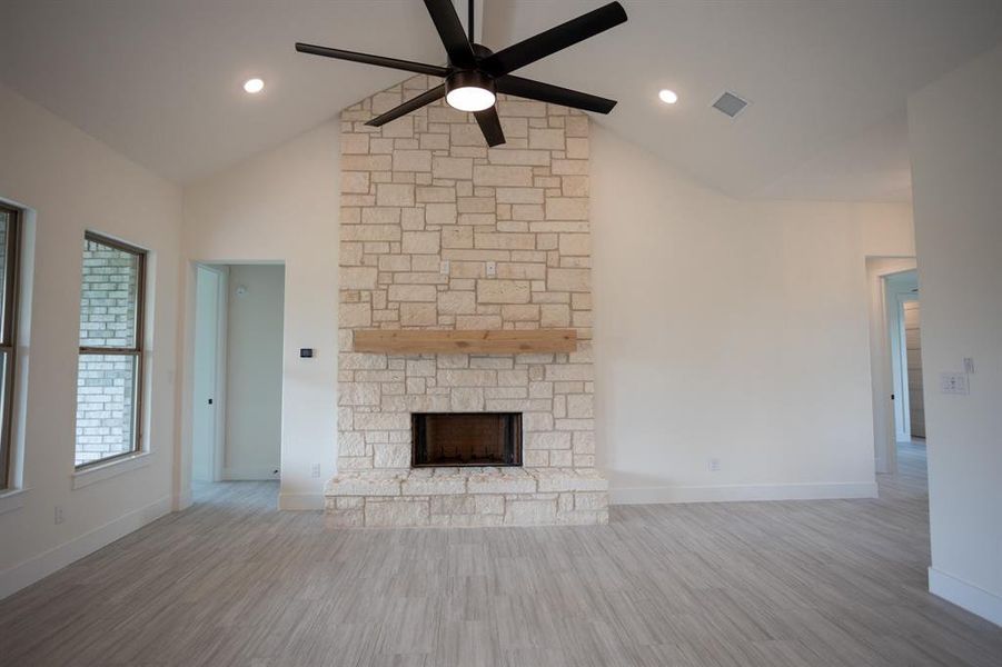 Unfurnished living room featuring wood finished floors, a fireplace, high vaulted ceiling, and ceiling fan Unfurnished living room featuring wood finished floors, a fireplace, high vaulted ceiling, and ceiling fan