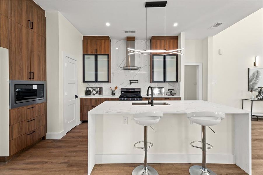 Kitchen with light stone countertops, a breakfast bar area, a center island with sink, modern cabinets, and two tone cabinetry