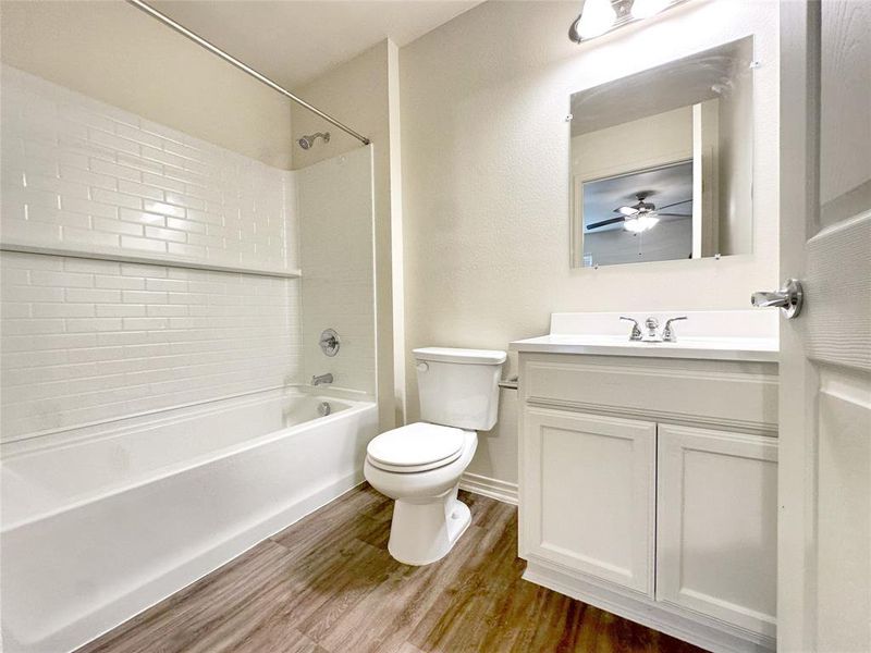 Full bathroom featuring vanity, tiled shower / bath combo, toilet, ceiling fan, and hardwood / wood-style floors