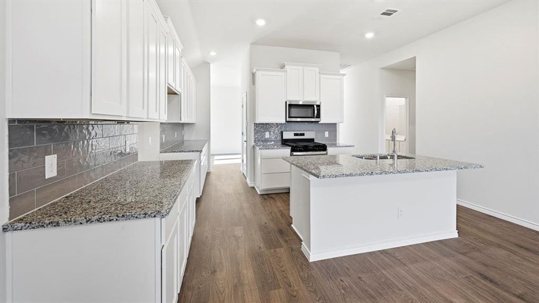 Kitchen featuring light stone countertops, white cabinets, a center island with sink, gas stove, and dark wood-style flooring